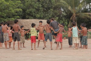 Foto composta por várias crianças em uma roda, de mãos dadas elas brincam.