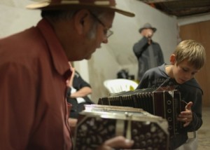 Foto de um senhor e um garoto, sentados eles tocam sanfona.