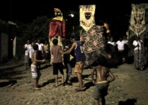 Foto ilustrando pessoas desfilando com bonecos grandes e bandeiras.