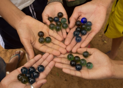 Foto ilustrando cinco mãos segurando bolinhas de gude, cada mão com sua quantidade.