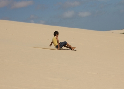 Foto com uma criança escorregando em uma montanha de areia.