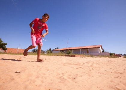 Foto com um garoto correndo em cima de duas metades de um cocô, cordas estão amarradas neste cocô a qual o garoto as segura.