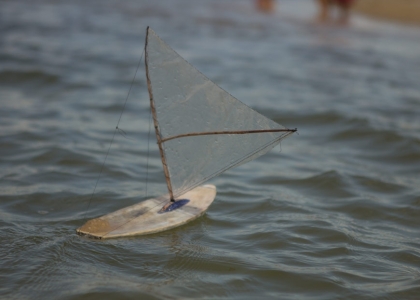 Foto ilustrando um barco a vela de brinquedo flutuando sobre as aguas.