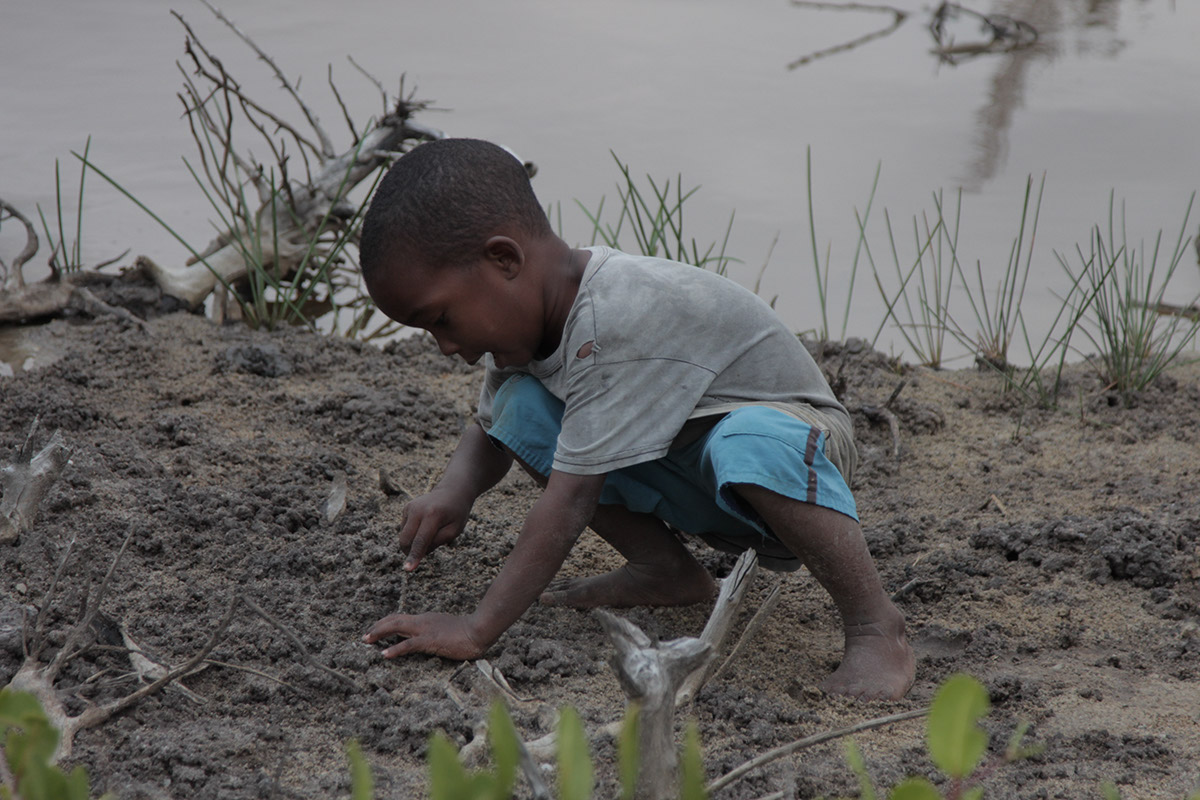 Foto de um garoto negro mexendo em um chão de terra.