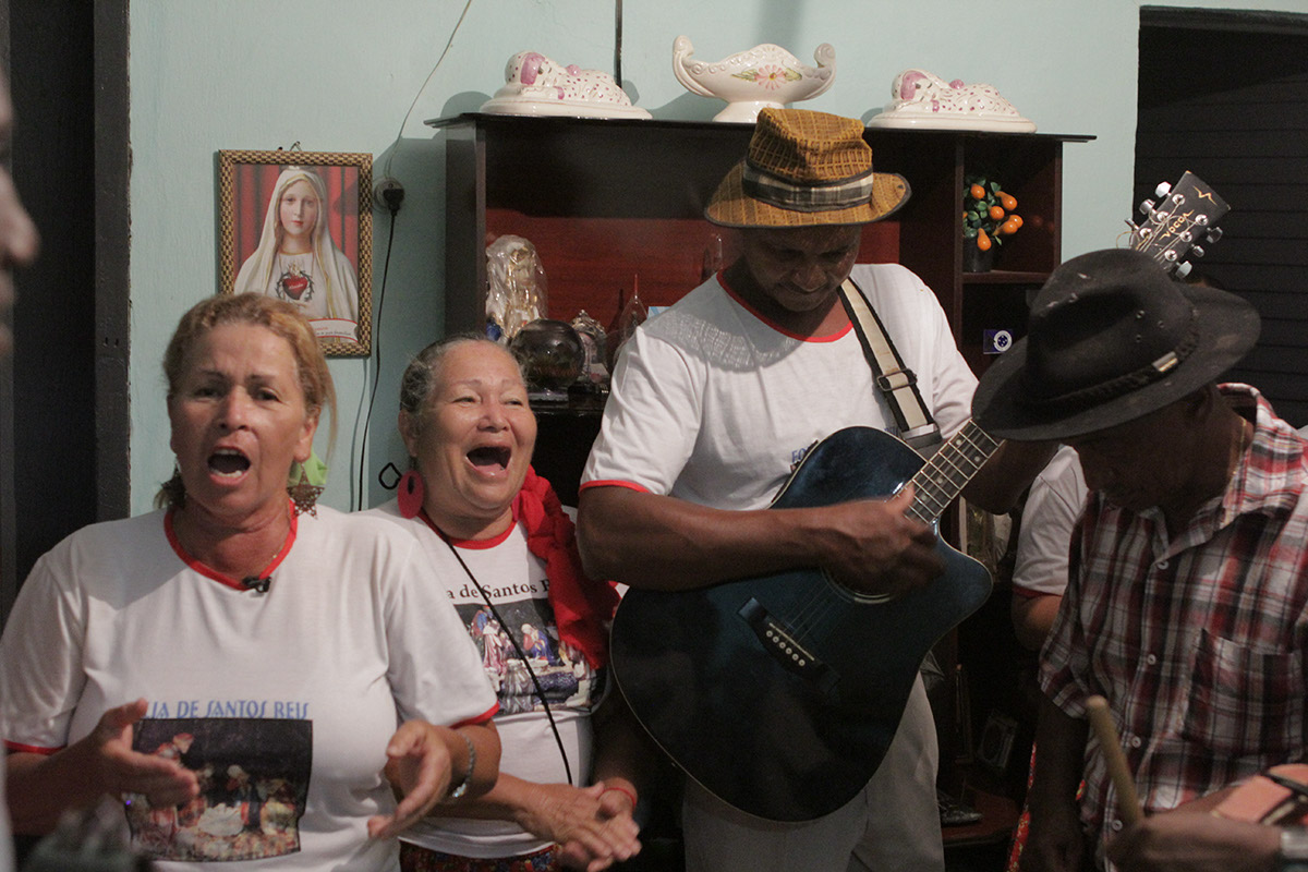 Foto de duas mulheres cantando e dois homens tocando instrumentos.