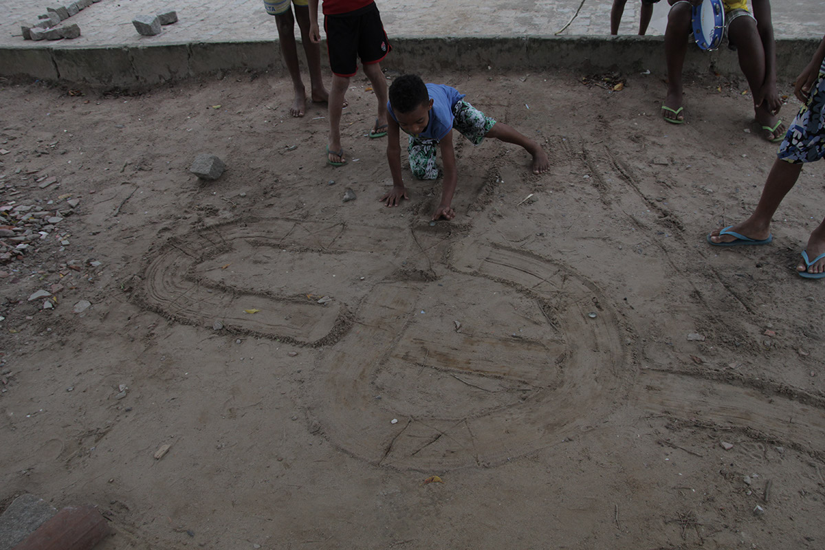 Foto de crianças brincando com uma tampinha em um chão de terra.