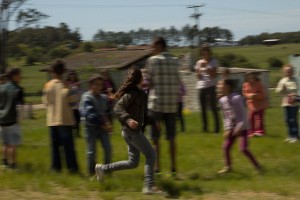 Foto com várias pessoas em uma roda, todas estão borradas, uma garota que tem o foco está correndo em volta destas pessoas.
