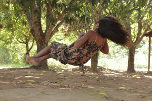 Foto de uma garota balançando de baixo de uma arvore ao entardecer do dia.