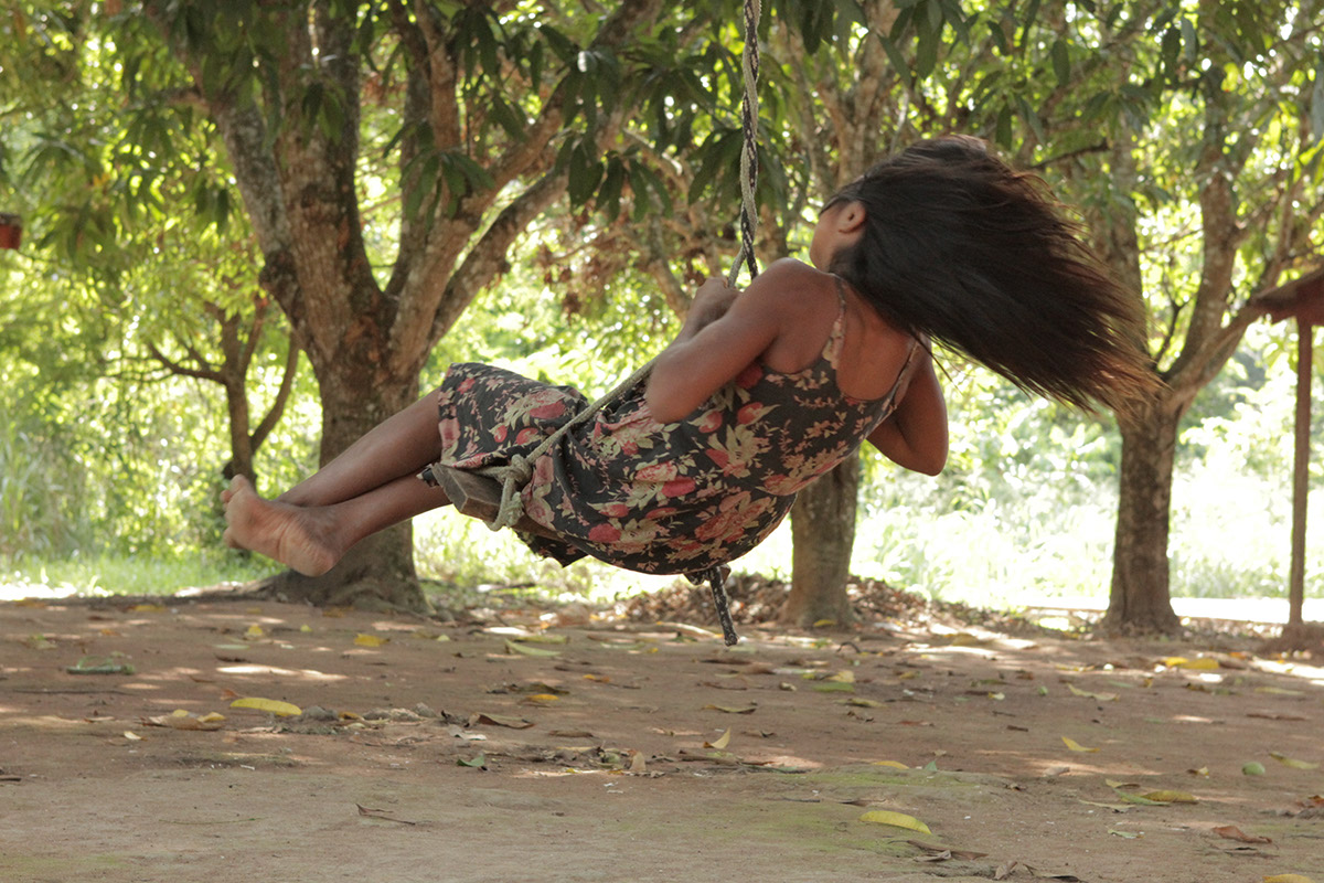 Foto de uma garota balançando de baixo de uma arvore ao entardecer do dia.