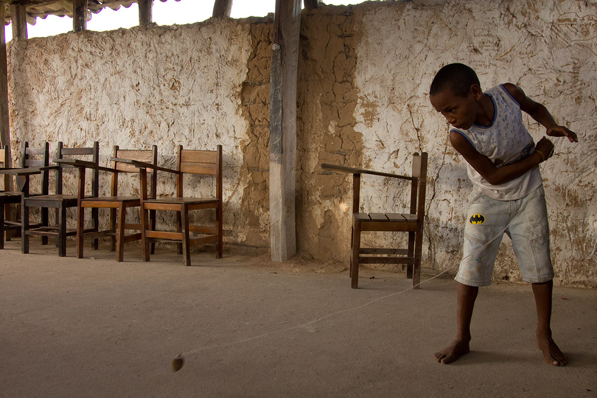 Foto com um garoto brincando de peão, onde logo após ter arremessado um peão, o garoto puxa a corda.
