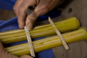Foto ilustrando um instrumento de brinquedo no colo de um homem, o brinquedo é feito de bambu.