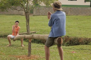 Foto de dois garotos brincando em uma gangorra feita com um tronco de madeira, um garoto tem um boné azul e outro usa um chapéu marrom.