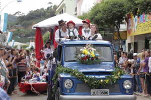 Foto de um desfile onde, pessoas estão em cima de uma caminhonete azul.