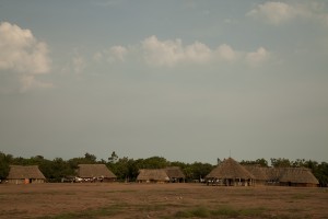 Foto ilustrando uma pequena vila com casa com teto de palha e estrutura de madeira.