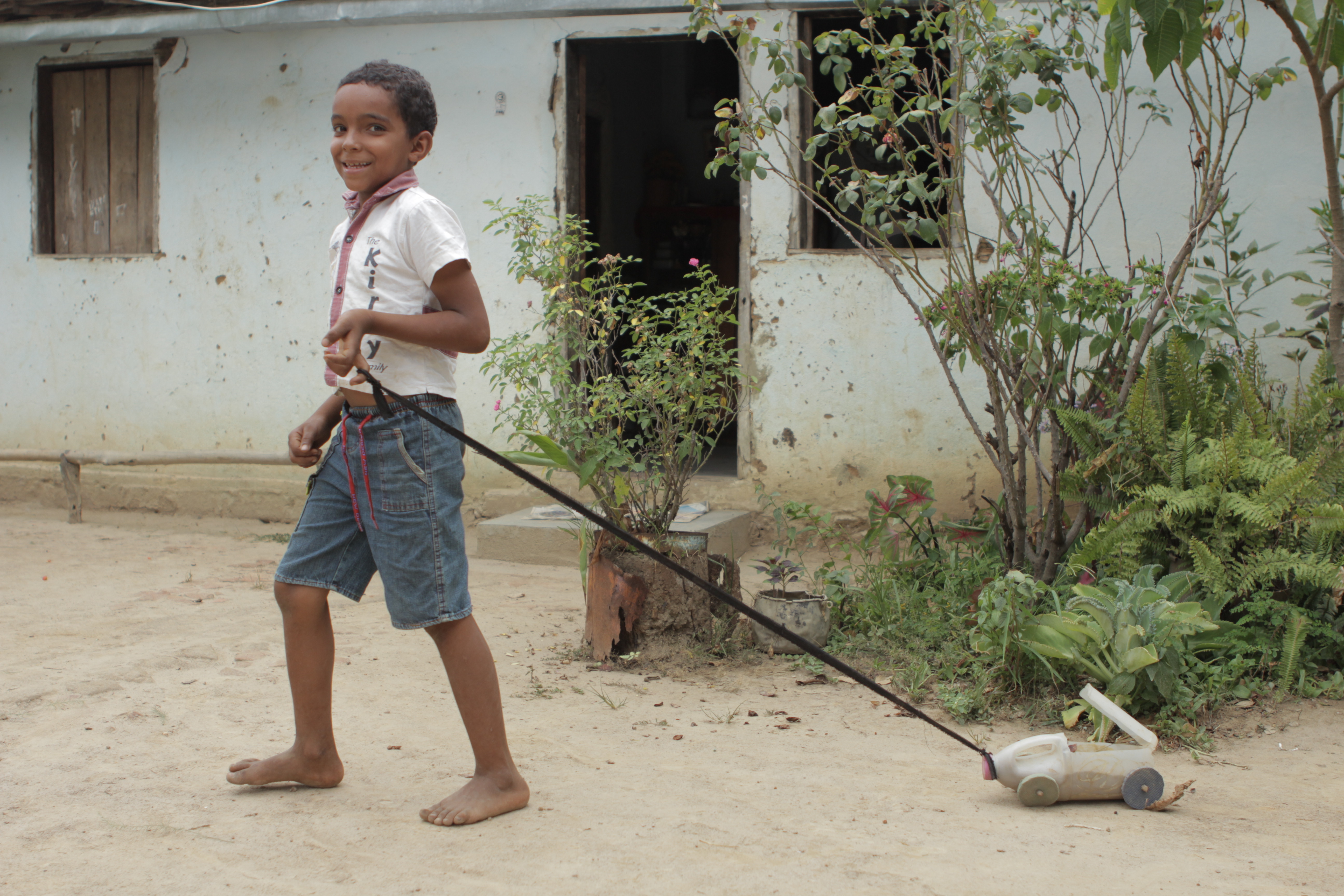 Foto com um garoto puxando um carrinho feito de uma garrafa de alvejante, o garoto puxa com uma corda amarrada.