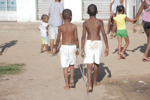 Foto de dois garotos negros sem camisa de bermuda branca estão amarrados em seus pulsos uma corda, ambos estão andando.
