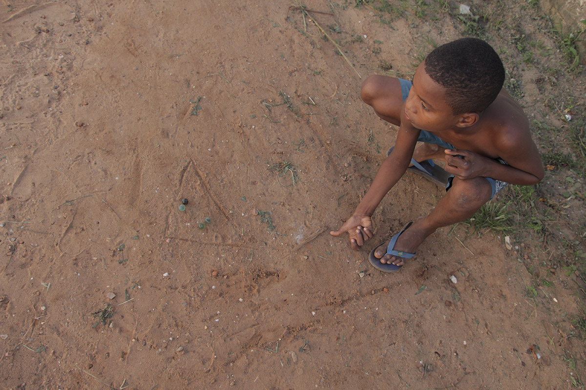 Imagem de um garoto ao chão brincando com bolinhas de gude.