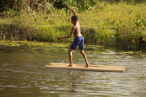 Foto de um garoto brincando sob uma madeira em um rio.