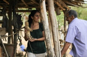 Foto com duas pessoas, uma mulher que segura um boneco de madeira enquanto olha para um senhor que vem em sua direção.
