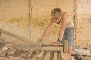 Foto de um garoto, inclinado encaixa a roda de um carrinho de madeira feito a mão.