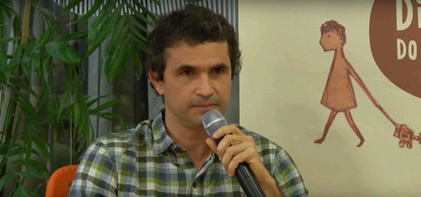 Foto de um homem sentado falando ao microfone.