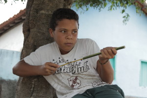 Foto de um garoto em baixo de uma arvore, ele está brincando.