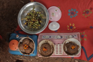 Foto de dois fogões de plástico com pratos de lama, tem uma tigela de alumínio com várias sementes ao lado.