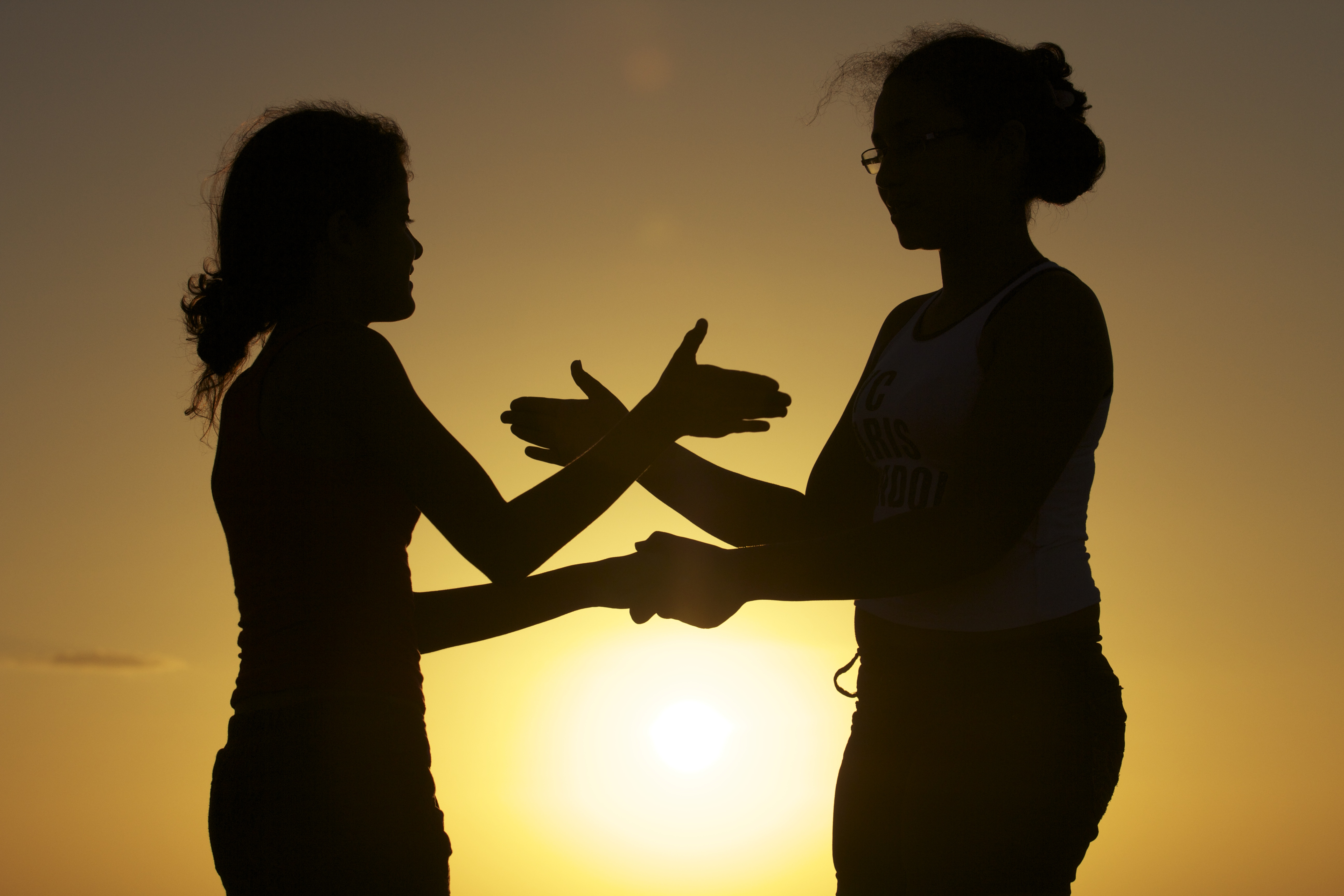 Foto de silhueta de duas meninas brincando de adoleta ao pôr do sol.