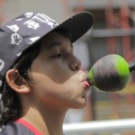 Foto de um garoto de boné preto segura um peão verde com a boca.