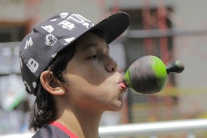 Foto de um garoto de boné preto segura um peão verde com a boca.