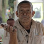 Foto de um senhor segurando um peão enquanto gira em sua mão direita.