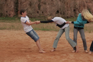Foto ilustra crianças brincando de mãos dada, um garoto em frente de todo mundo puxa o resto.