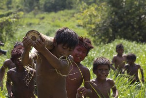 Foto composta por vários garotos carregando tronco e andando em meio ao mato.