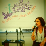 Foto de uma senhora sentada em uma cadeira, fala ao microfone.