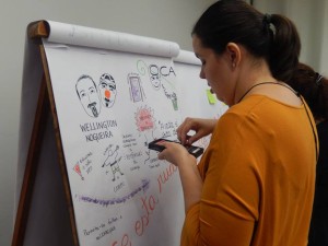 Foto ilustrando uma mulher escolhendo giz de cera para escrever em um quadro em sua frente.