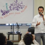 Foto de um home de barba falando ao microfone em cima de um palco.