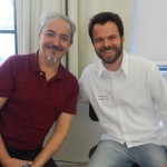 Foto com dois homens sentados um é grisalho.