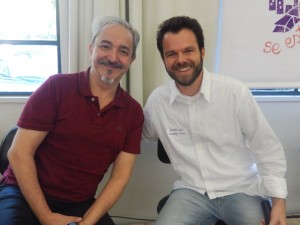 Foto com dois homens sentados um é grisalho.