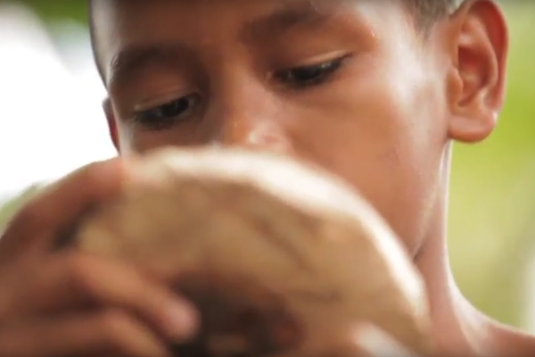 Foto de um garoto segurando e observando uma talha de madeira.