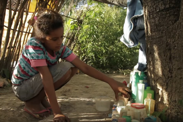 foto de uma menina abaixada, brincando com vários frascos em baixo de uma arvore.