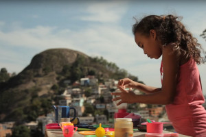 Foto de uma garota brincado de chá com uma mesa posta com várias peças de plástico, a garota serve o chá.