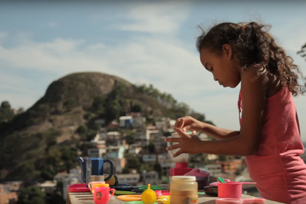 Foto de uma garota brincado de chá com uma mesa posta com várias peças de plástico, a garota serve o chá.