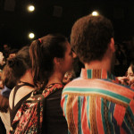 Foto de um grupo de pessoas de costas assistindo á um evento.