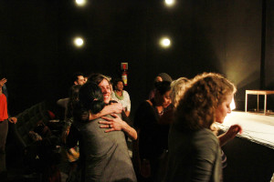 Foto mostrando inúmeras pessoas se interagindo , onde há abraços e comprimentos ao centro da imagem entre duas mulheres.