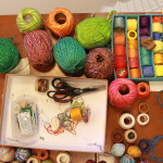 Foto de uma mesa com inúmeras linhas de costura de diversas cores , junto com algumas tesouras e agulhas