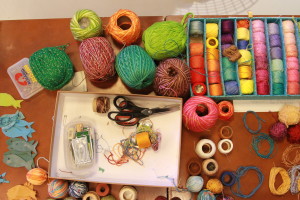 Foto de uma mesa com inúmeras linhas de costura de diversas cores , junto com algumas tesouras e agulhas