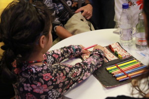 Foto de uma criança brincando com um estojo de lápis de cor que estão encima de uma mesa.