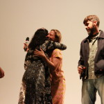 Foto com quatro pessoas , onde ao centro á duas mulheres se abraçando.