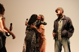Foto com quatro pessoas , onde ao centro á duas mulheres se abraçando.