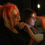 Foto ilustrando interação entre pessoas , onde á duas mulheres ao centro da foto assistindo uma palestra.